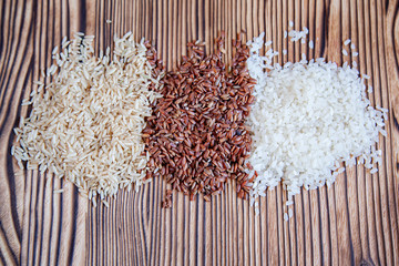 Different types of rice on a wooden background. White, brown and red.