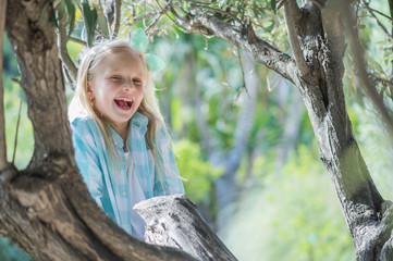 Happy girl sitting in a tree and enjoying the view. Summer time fun