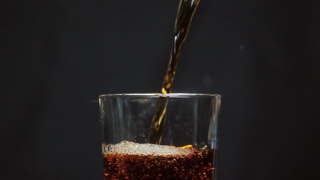 Pouring carbonated drink close up. Cola with bubbles in a glass. Coke soda close up. Food background. glass of cola fizzy drink on a black background. Slow motion