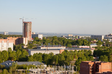 Fototapeta premium Nowe osiedle w środku starej zabudowy i zieleni na tle budowanego wielokondygnacyjnego budynku i dźwigu.