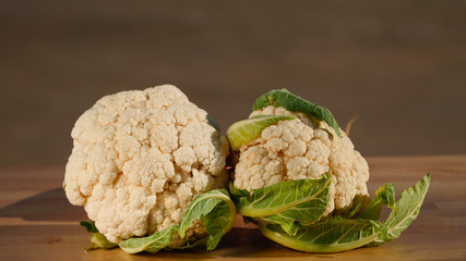 Closeup of two fresh organic cauliflowers on wooden table, brown background, healthy diet