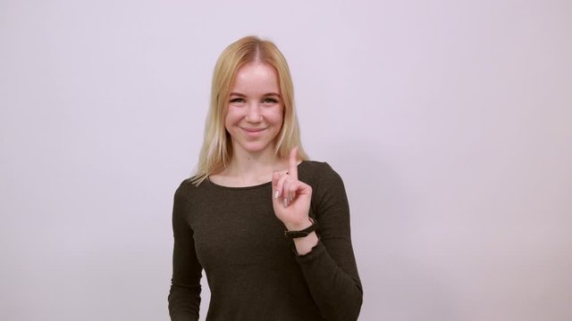 Young Blonde Woman In Black Sweater With Stylish Watch On White Background, Happy Attractive Girl Smiling Points forefinger At The Person In Front. Concept Of Guilty People And Charges