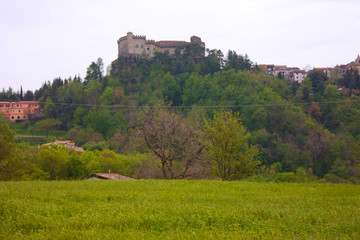a feudal castle of the Lunigiana in the distance on the hill among the green fields on a cold day and gray sky