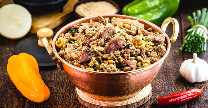 "Feij&atilde;o tropeiro", typical Brazilian food, in copper pot, rustic cuisine, with ingredients and vegetables in the background.