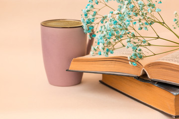 An open book with a glass of coffee on a light background. On the book is a branch with small, blue flowers. Side view. Space for text. Horizontal photo.