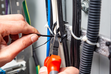 Hands with wire cutters cut the ties from the wires on the cable tray.Close-up. Horizontal...