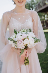 Bride's bouquet close-up, the bouquet consists of white and pink peonies, eucalyptus. The bride dressed in pink wedding dress holds the bouquet 