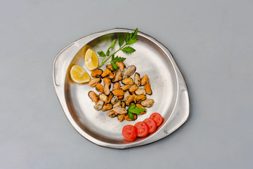Mussels without shell with tomato slices and lemon on a steel tray. Seafood concept. Top view. Space for text