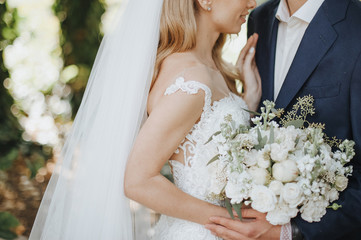 Close-up of a bride’s bouquet of white flowers. The bride in a lace white dress holds a bouquet...