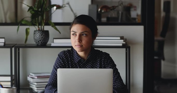 Serious young indian businesswoman student or worker using laptop computer tech working from home. Ethnic professional female employee thinking searching ideas looking away doing online job in office.