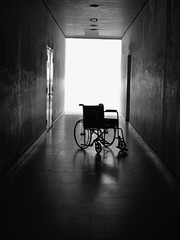 Fototapeta na wymiar Low key images of an empty wheelchair in an empty hallway - sickness or loneliness in a hospital concept.