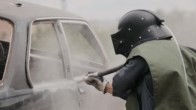 The worker cleans the cars elements by sanding. Sandblasting of metal surface of the car by compressed air of the sandblaster gun