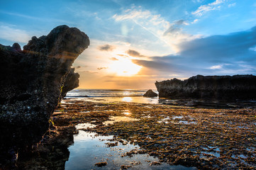Amazingly beautiful long exposure sunset on the coast of Canggu, a resort village on the south coast of the Indonesian island of Bali. Rocks covered with seaweeds, reflection in the water.