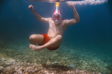 Snorkeler, snorkeling man in full face mask, summer vacation activity, swimming in the warm tropical sea, seashore and fishes, starfishes near rocks, Italy