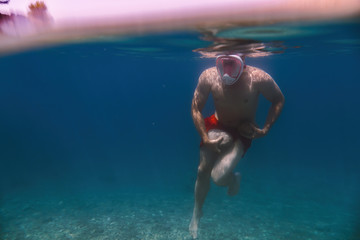 Snorkeler, snorkeling man in full face mask, summer vacation activity, swimming in the warm tropical sea, Doing sports. Walking on the bottom. Stones hold cargo. Copy space