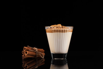 Iced Dalgona coffee in beautiful glass with spices. A trendy fluffy creamy whipped coffee. Korean coffee drink on a black glass table with reflection. Close-up, copy space