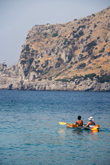 A group of tourists on excursions, kayak rental and sightseeing guide. Active leisure and sport. Back view. Vertical photo. Cliffs and mountains in the background.