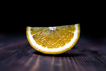 A slice of orange lies on a wooden surface on a dark background. Grunge texture background. Poster design. Nature background. Sweet fruit. Design element. Concept of product design. Tropical fruit