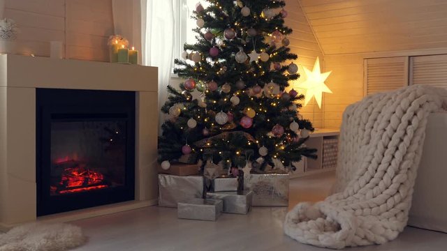 Christmas celebration in cozy interior with decorated new year tree, fireplace and merino plaid. Evening time. Winter holidays