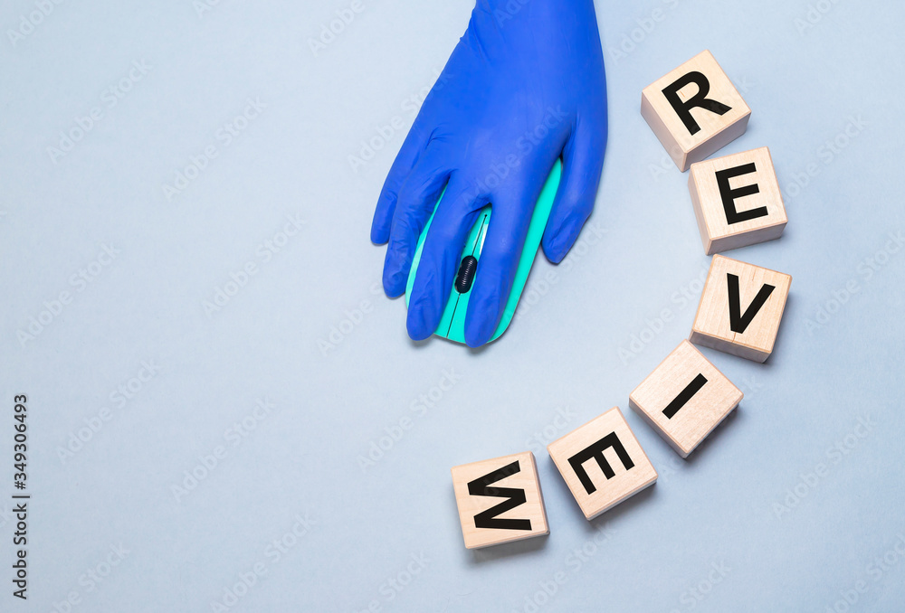 Poster word review written on wooden cube blocks with hand in protective glove on a computer mouse on blue 