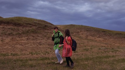 Fototapeta na wymiar free female travelers go to gorge, holding hands. teamwork travelers. Healthy tourist girls travel with backpacks in colorful raincoats, storm is approaching. concept of adventure and travel.