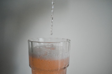 Transparent, pinkish gaseous liquid, falling into a crystal glass foaming