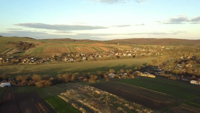 Aerial view of countryside village with small houses among green trees with farm fields and distant forest in summer.