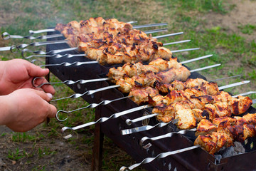 The male hand flips the finished pork skewers on skewers. Cooking meat on a fire in nature