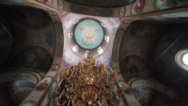 The interior in the Orthodox Church. Painted walls and ceilings, arches, icons, a gold chandelier and a dome
