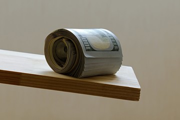 bundle of dollars rolls onto the edge of a wooden board