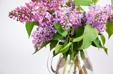 Bouquet of flowering branches of lilac on a light background close-up. Home interior with decoration elements.