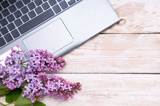 The workplace of a freelancer or blogger with a keyboard. Blossoming branches of lilac and laptop on a light wooden table.