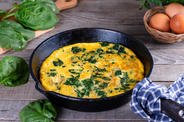 Omelet with spinach in the pan on the wooden table