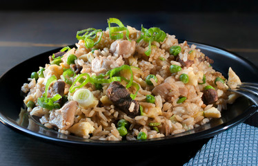 Chinese food traditional chicken and beef fried rice on a black plate with a blue napkin on the side and a dark wooden table with a black background. Close up