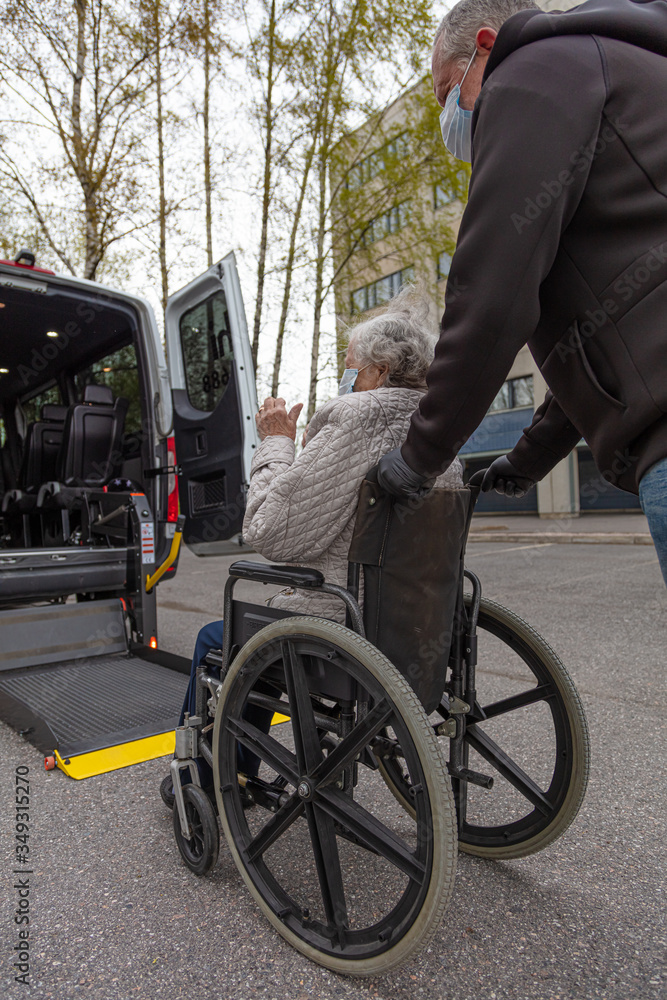 Wall mural Handicapped person loading in a wheelchair into a minibus for transportation.
Male driver and elderly woman in medical masks.