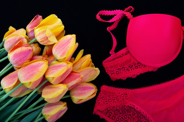 A bouquet of orange-red tulips and bright red women underwear(bra and pantie) on black background.Romantic lingerie.Flat lay.Сoncept of women`s holidays,erotic gifts for your beloved.