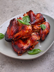 Grilled chicken wings in soy sauce decorated with basil in a plate on a concrete background