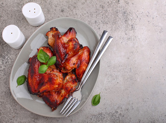 Grilled chicken wings in soy sauce decorated with basil in a plate on a concrete background, top...