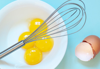 The whisk over fresh raw chicken yolks, eggs shells on the blue background. Baking or food...