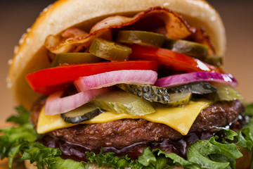 Delicious juicy burger with beef patty, bun and vegetables on a serving wooden board with a knife stuck. Food delivery. Fast food restaurant.