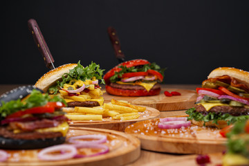 Fototapeta premium A set of different burgers. Fast food restaurant board. A diverse snack menu. Serving on a wooden board on a black background.