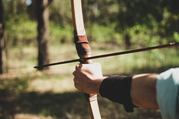 A man shoots a bow in the open air. The near foreshortening. An arrow is pulled over the bow.

