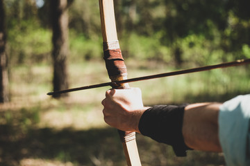 A man shoots a bow in the open air. The near foreshortening. An arrow is pulled over the bow.
