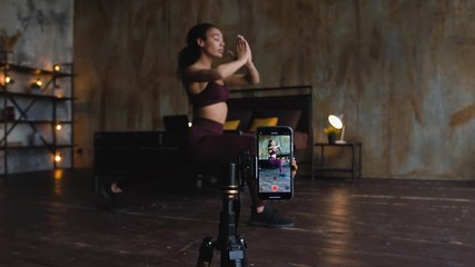 Young attractive african american woman blogger recording video with a smartphone live streaming doing sport exercises in bedroom at home. Quarantine workout concept. Dolly shot