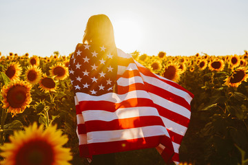 4th of July. Nice girl with the American flag in a sunflower field.Freedom. Sunset light....