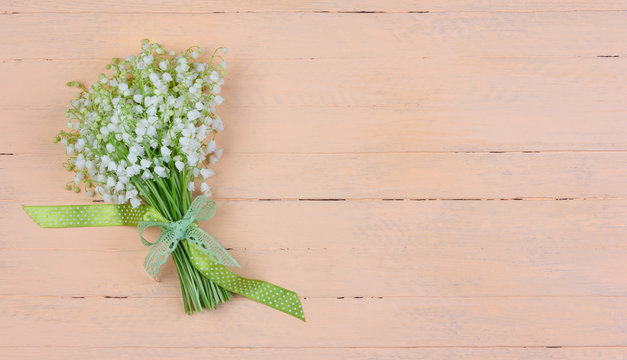 A bouquet of fragrant Lily of the valley flowers with a green and white polka dot bow on a pink wooden background with a copy space, top view