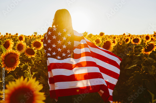 4th of July. Nice girl with the American flag in a sunflower field.Freedom. Sunset light. Independence Day. Patriotic concept.