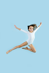 Happy little girl in a white leotard doing gymnastic form in a jump over blue