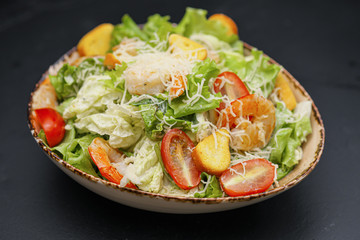 Caesar salad with shrimp in a bowl on a black background.