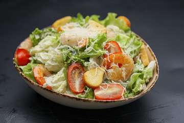 Caesar salad with shrimp in a bowl on a black background.